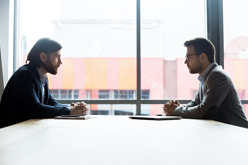 Shot of two coworkers talking together while standing in a large modern office