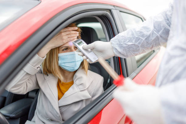 istock Medic using hand held infrared thermometer for a woman driving a car 1309116447