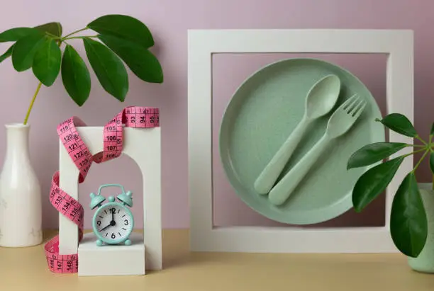 Photo of Trendy composition with plate, spoon, fork, alarm clock, meter, decorative figures and leaves.