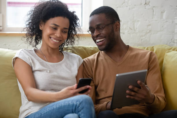 istock Happy smiling mixed race couple relaxing at home using gadgets 1309117501
