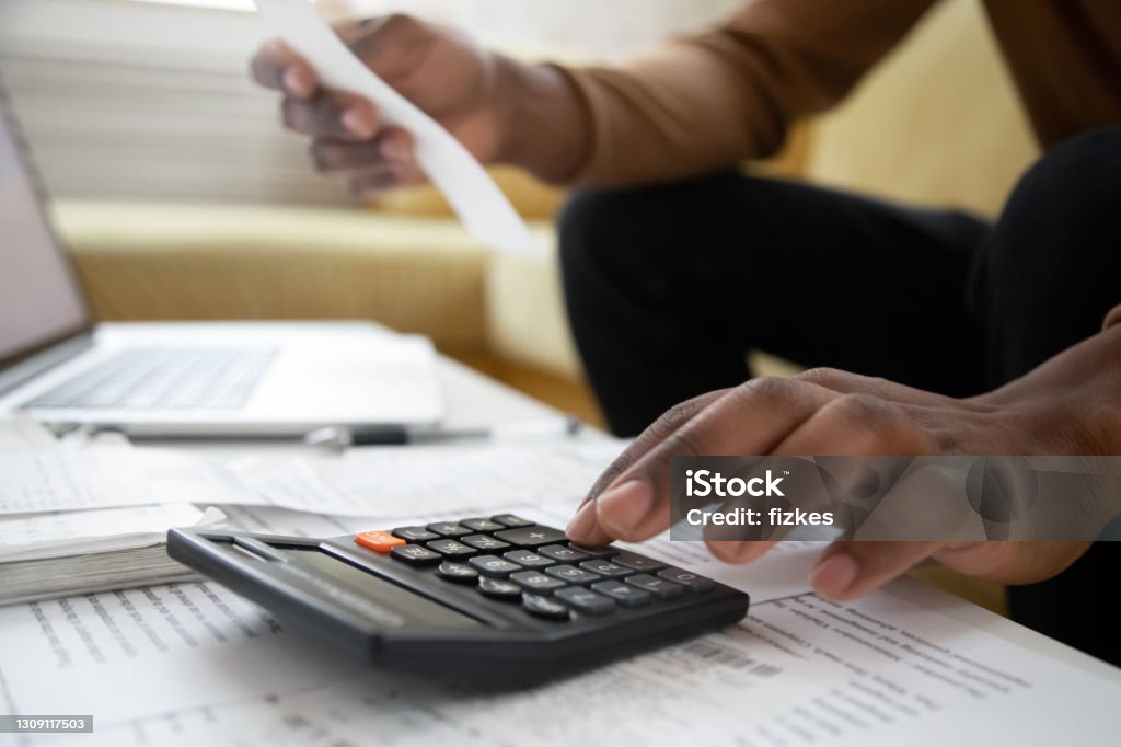 Close up of african american man with calculator checking bills Close up of african american man with calculator checking bills at home. Savings, finances, economy concept. Black small business owner calculating income and planning budget Home Finances Stock Photo