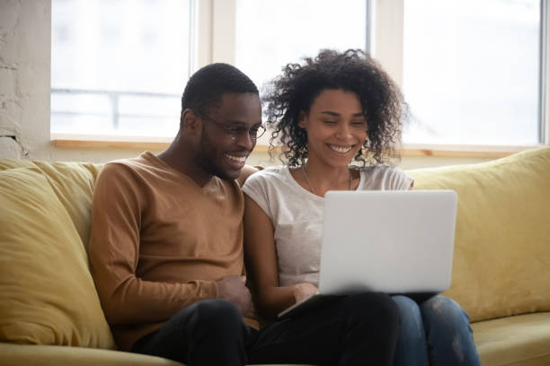 Happy black couple speak with friends online distance video call Happy black couple speak with friends online making video call. Smiling mixed race married man and woman sitting on coach in living room use laptop for distance conference calling mixing stock pictures, royalty-free photos & images