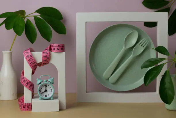 Photo of Trendy composition with plate, spoon, fork, alarm clock, meter, decorative figures and leaves.