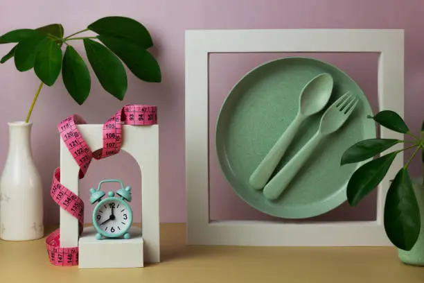 Photo of Creative composition with dishes, alarm clock, meter, decorative figures and leaves.