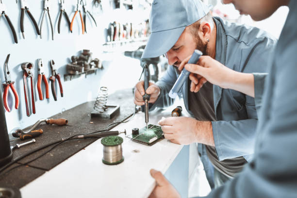 apprentice holding light for senior electrical engineer soldering car part - men baseball cap focus determination imagens e fotografias de stock