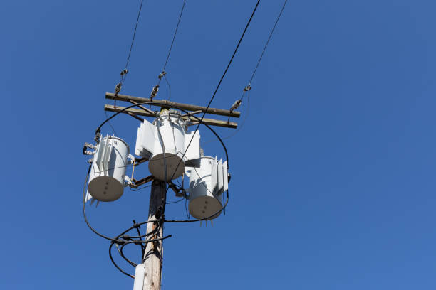 Tall wood electric pole with three transformers against a clear, deep blue sky, horizontal aspect
