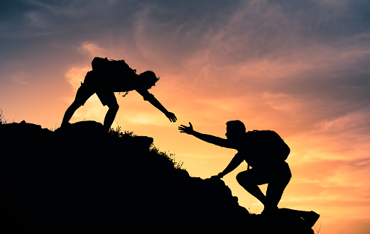 Two male hikers helping each other climb up a mountain. Teamwork and perseverance.