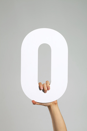 A hand holding the letter O or zero.
