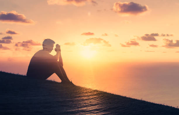 Man making praying hands in a beautiful sunrise setting. Religious belief concept. Double exposure sunrise timelapse stock pictures, royalty-free photos & images