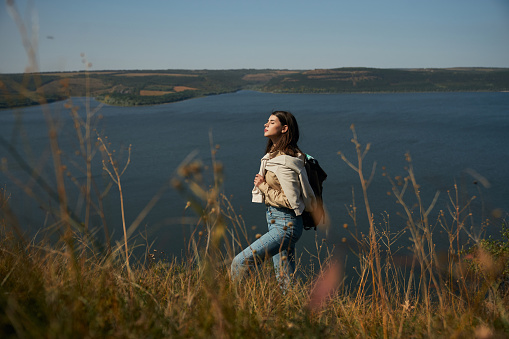 Pretty dark-haired woman standing on mountain peak with closed eyes and enjoying fresh air at national ukrainian park. Concept of people, hobby and adventure.