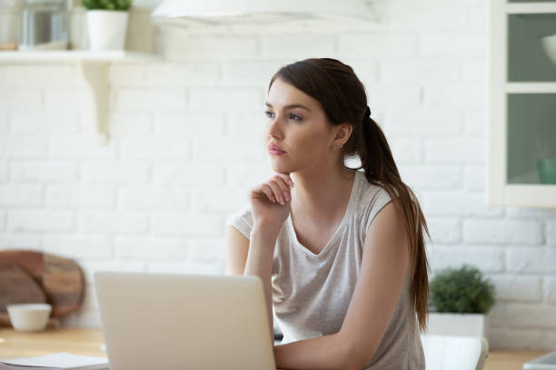 istock Dreamy thoughtful woman sitting at table with laptop in kitchen 1309122619