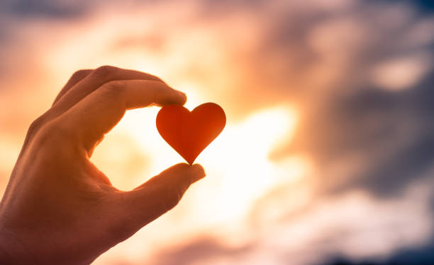 istock Hand holding little red heart against sunset. 1309122662