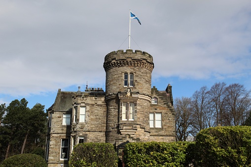 Edinburgh, Scotland - 25 March 2021 Old stone manor house behind shrubs with a Scottish saltire on flagpole