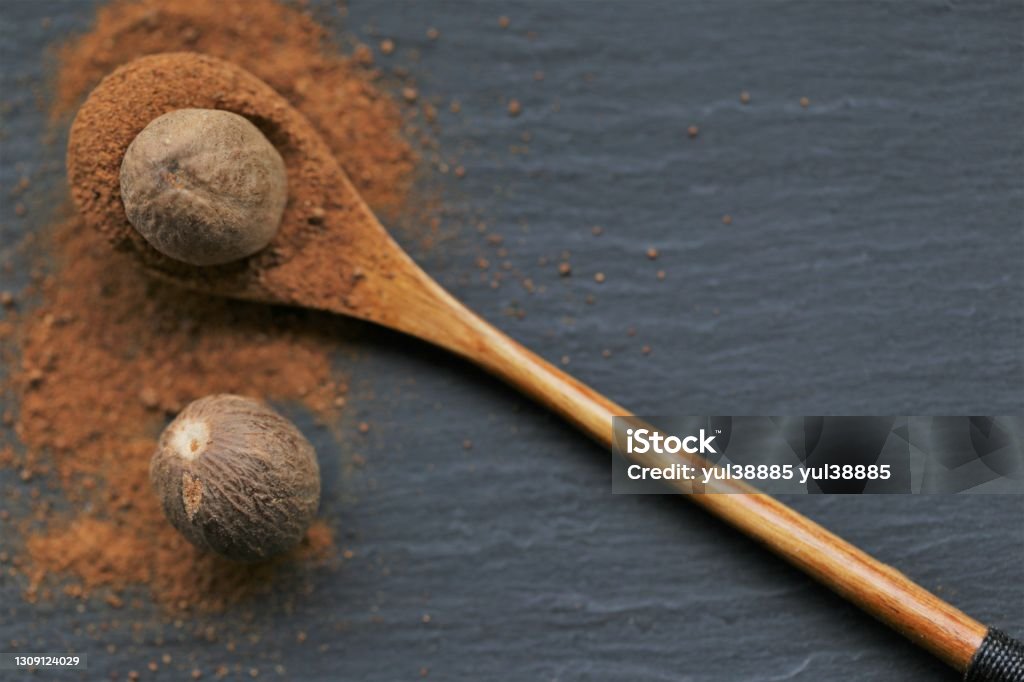 Nutmeg spice.Whole and ground nutmeg in a wooden spoon close-up on a black schiffer background.Spices and herbs concept.Food .Spices for meat and baking.Nutmeg powder Baking Stock Photo