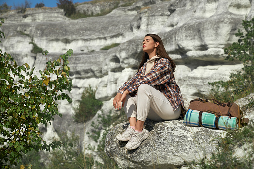 Young woman with brown hair relaxing on rock, keeping her eyes closed and enjoying favorite hobby outdoors. Pretty lady spending active leisure time at national ukrainian park.