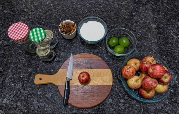 Red apples in glass bowl, cinnamon sticks and utensils for making homemade jam