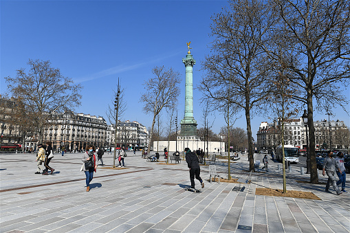 Paris, France-03 23 2021: Walking and sitting people in place de la Bastille in Paris.The Place de la Bastille is a square where the Bastille prison stood until the storming of the French Revolution.No vestige of the prison remains.The July Column stands at the center of the square.