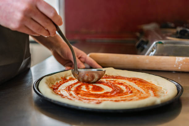 istock Close-up of chef using ladle to spread sauce on a pizza 1309126564