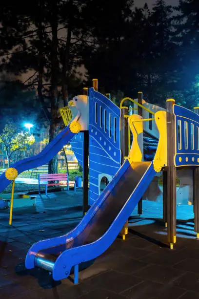 Playground in a park at night. Blue nightlights, trees in the background. Chisinau, Moldova