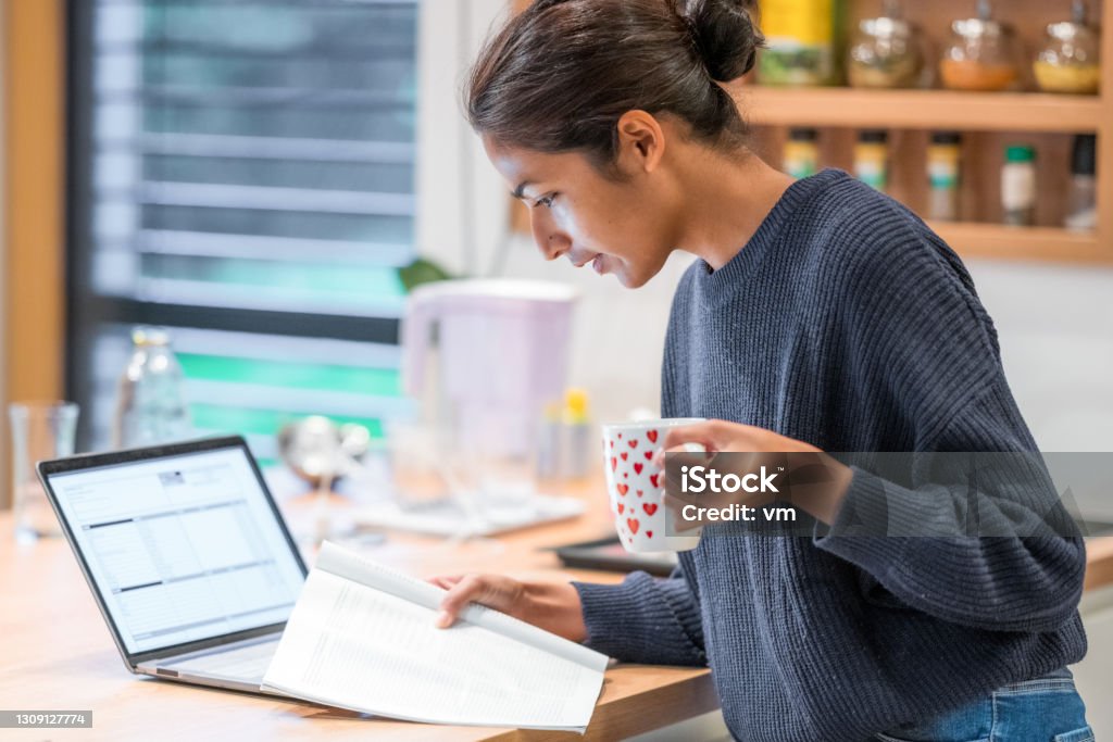 Woman standing in kitchen and reading brochure Woman standing in kitchen and reading brochure. Holding cup of tea. Using modern technology, home office, distance education concept. Home Office Stock Photo