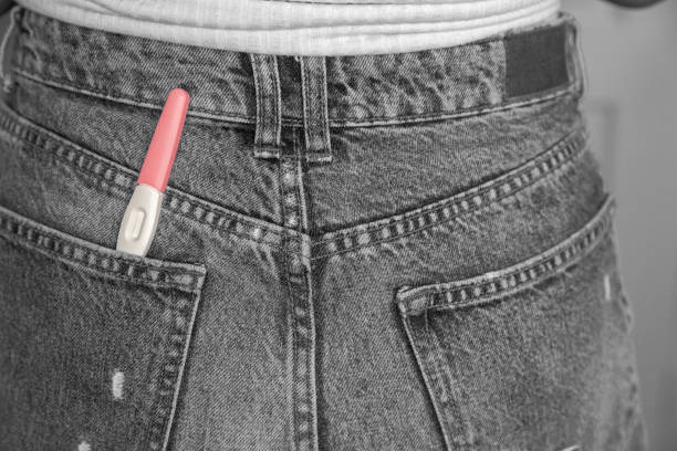 Young woman with positive pregnancy test in pocket of jeans close-up black and white Young woman with positive pregnancy test in pocket of jeans close-up motherhood happiness modern retro background couple hope sky blue stock pictures, royalty-free photos & images