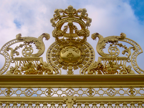 Horizontal closeup photo of the beautiful gold-painted front entry fence at the Palace of Versailles with ornate decoration panels.