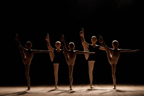 istock Flexible ballerinas stretch on a dark lighted scene. 1309135942