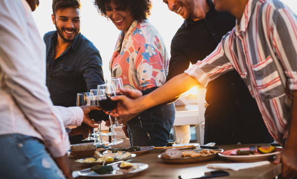 jeunes amis grillant avec le vin rouge à l’heure de coucher du soleil d’apéritif sur la maison de patio - concept de boisson et de nourriture - wine dinner party drinking toast photos et images de collection