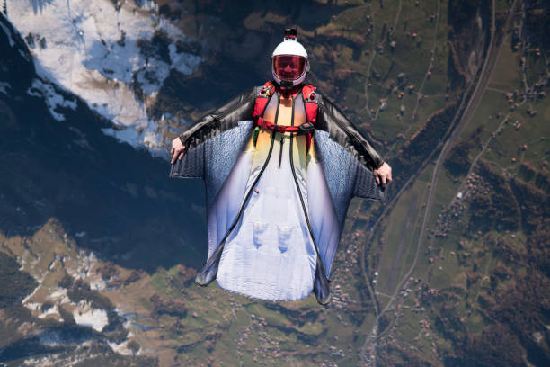 le costume d’aile s’élève au-dessus du paysage de montagne - wingsuit photos et images de collection