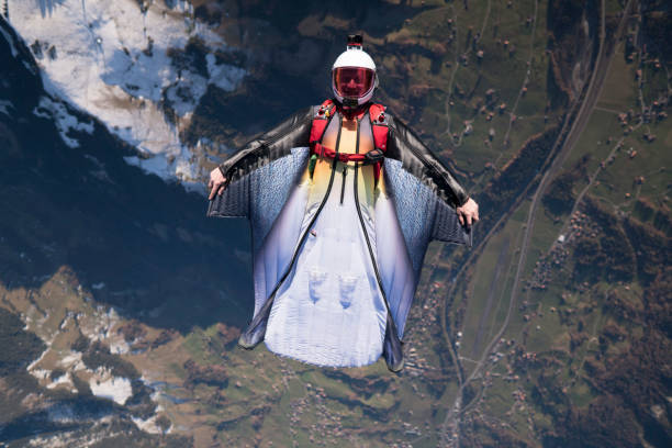 Wing suit soars above mountain landscape Snow capped peaks below gliding stock pictures, royalty-free photos & images