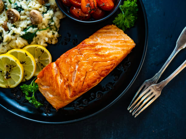 istock Fried salmon steak, risotto with white mushroms and roasted tomatoes on wooden black table 1309147559