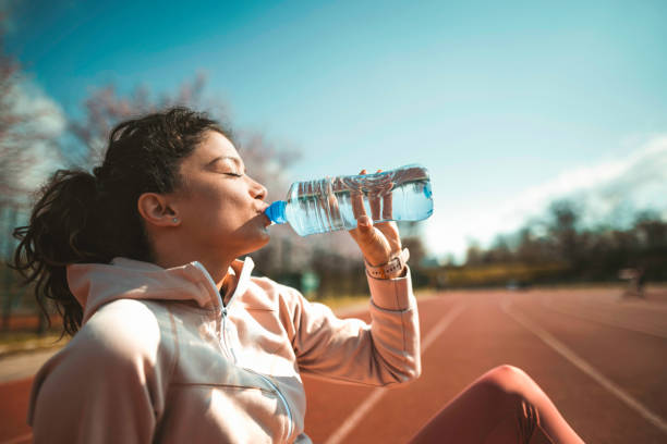 sportliche junge frau trinkwasser nach dem laufen auf der sportbahn. - running track women running spring stock-fotos und bilder