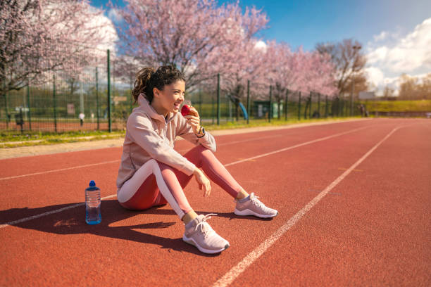 glückliche junge sportlerin, die einen apfel auf der sportbahn isst. - sport food exercising eating stock-fotos und bilder