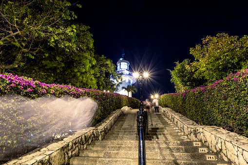 View of the steps at the main route through houses, stores and restaurants at Las Peñas neighborhood, leading to the top of the Santa Ana hill, the lighthouse visible in the background