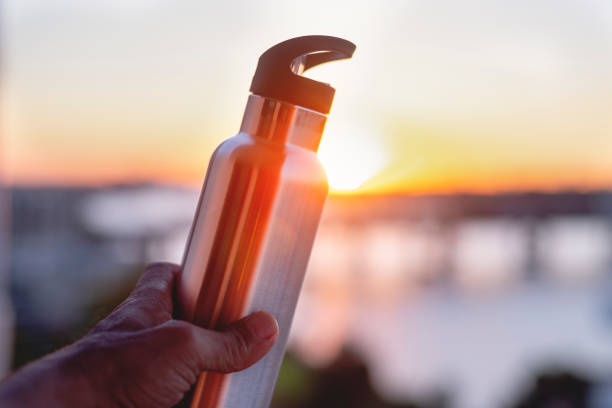 Man holding up a metal reusable water bottle at sunset.