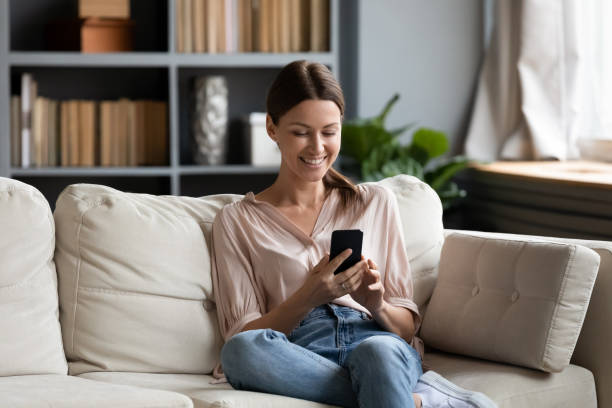 istock Smiling woman looking at smartphone screen, sitting on couch 1309167689