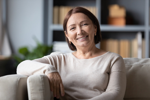 Head shot portrait smiling mature woman sitting on cozy couch