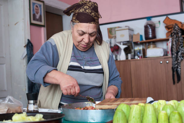 An old woman is carving an eggplant with a zucchini carving tool to make stuffed vegetables.