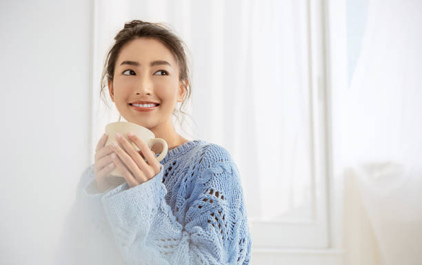 그녀의 흰색 침실에서 커피 아침 겨울 시간 한 잔을 들고 젊은 아름다운 아시아 여성의 초상화. 추운 겨울에 행복한 hygge 쾌활한 휴식, 바리스타 컨셉 배너 - winter beauty cold women 뉴스 사진 이미지