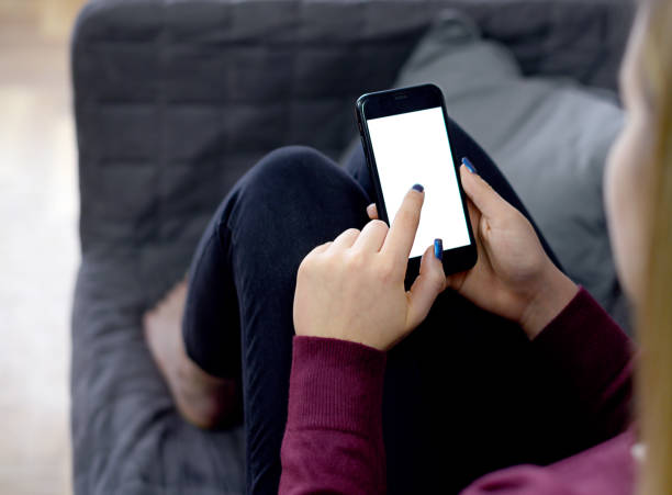 istock Back view close up of a woman hand holding and using smart phone with white blank empty screen sitting on a bed at home. 1309200733