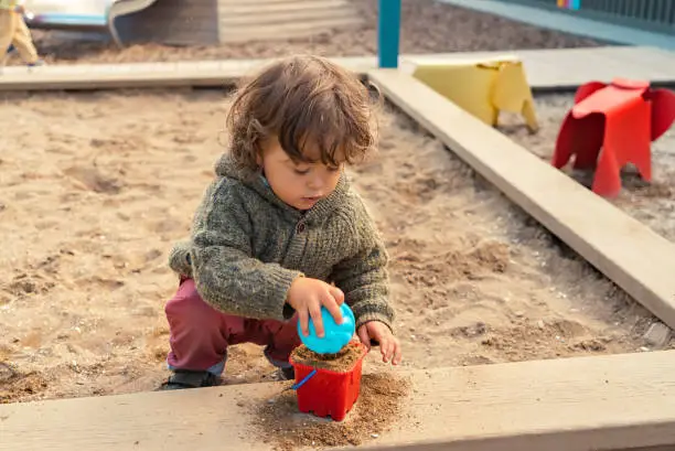 Portrait of a little boy with long hair playing in the sandbox at the playground outdoors
