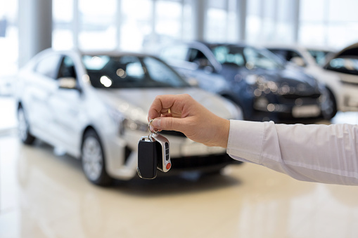 Salesman holding keys to a new car. Car auto dealership. Modern and prestigious vehicles.