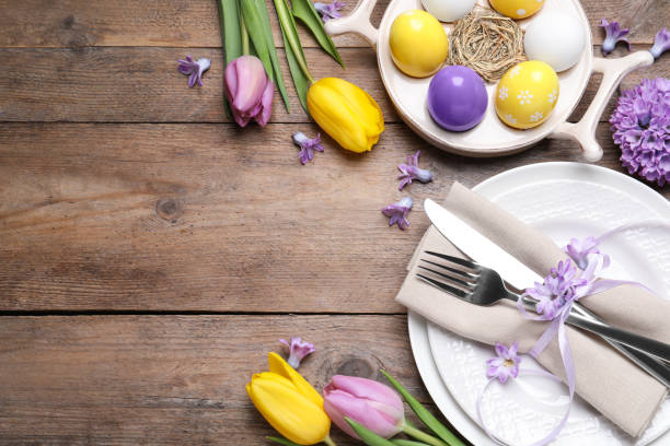 istock Festive Easter table setting with painted eggs and flowers on wooden background, flat lay. Space for text 1309213254
