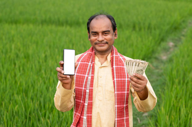 fermier indien affichant le téléphone portable et l’argent dans le domaine agricole vert - global village photos et images de collection