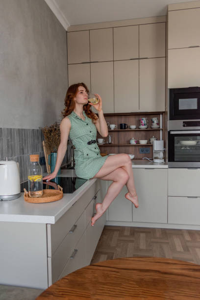 istock Young woman drinks water with lemon in a glass sitting at kitchen table. 1309224655