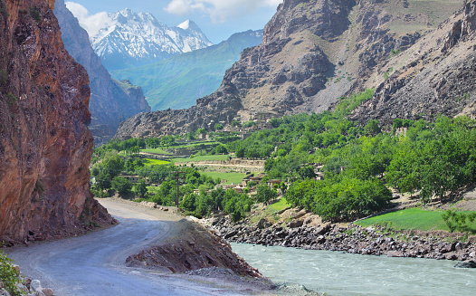 Road in a deep mountain gorge. Below is a tumultuous river Panj. Pamir Highway, Tajikistan. On the opposite bank of the territory of Afghanistan.