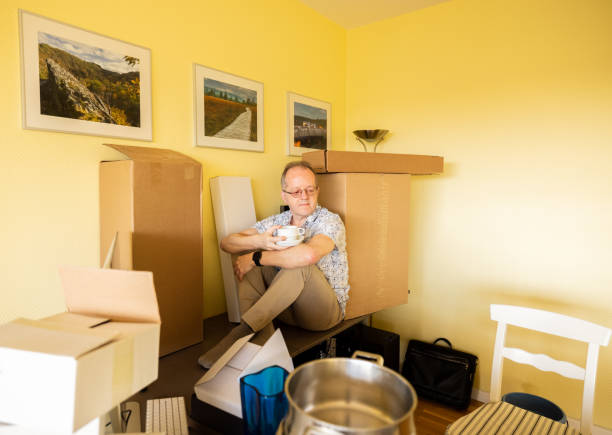 istock Senior single man in empty office apartment room, resting and taking a break from moving in or moving out, surrounded by cardboard boxes, drinking coffee 1309227362