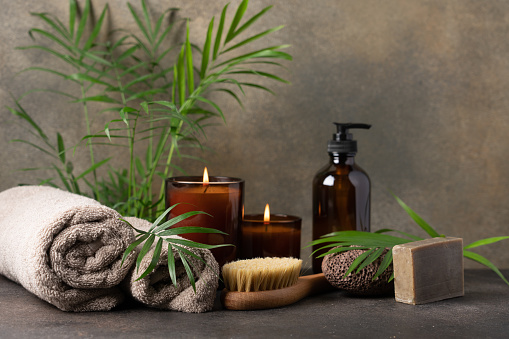 Сandles, towels, massage brush, volcanic pumice stone, care cream in dark glass bottle and green tropical plants. Beauty spa treatment and relax concept
