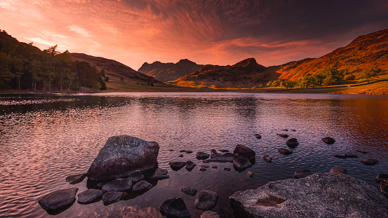 Sunset over Blea Tarn in Lake District, Cumbria, UK. Tranquil golden hour landscape scenery with Langdale pikes lit by setting sun. Beautiful nature background with atmospheric mood.