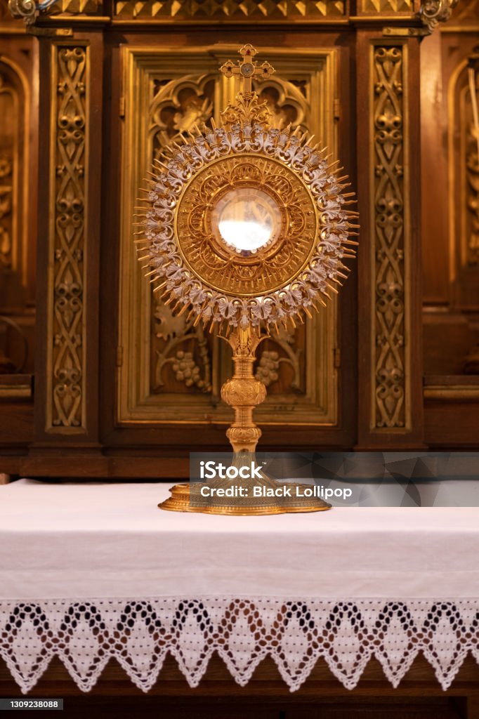 Golden ostensorium in the Roman Catholic Church. Close up on a beautiful monstrance (or an ostensory) in the shape of the sun standing on a retabl or altarpiece. Monstrance, also called ostensorium, in the Roman Catholic church is a vessel in which the eucharistic host is carried in processions and is exposed during certain devotional ceremonies. Ostensorium Stock Photo